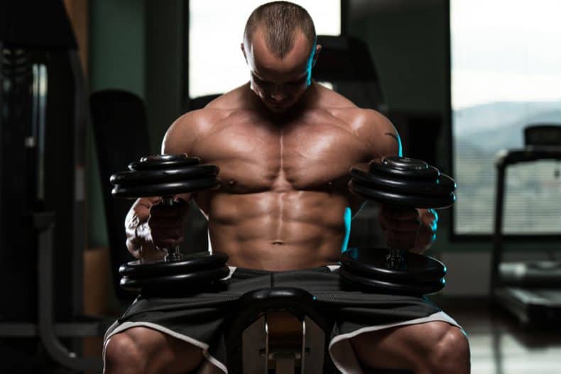 man sitting on flat weight bench with dumbbells