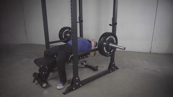 man performing bench press inside rack on rep fitness adjustable weight bench