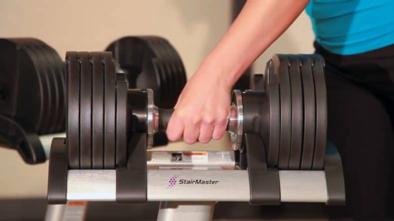 woman taking adjustable dumbbell from stand