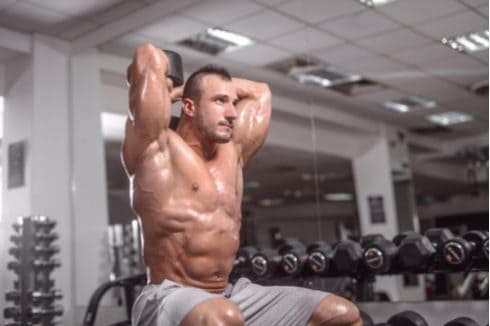 bodybuilder and dumbbells in gym male bodybuilder doing tricep extensions lean muscle
