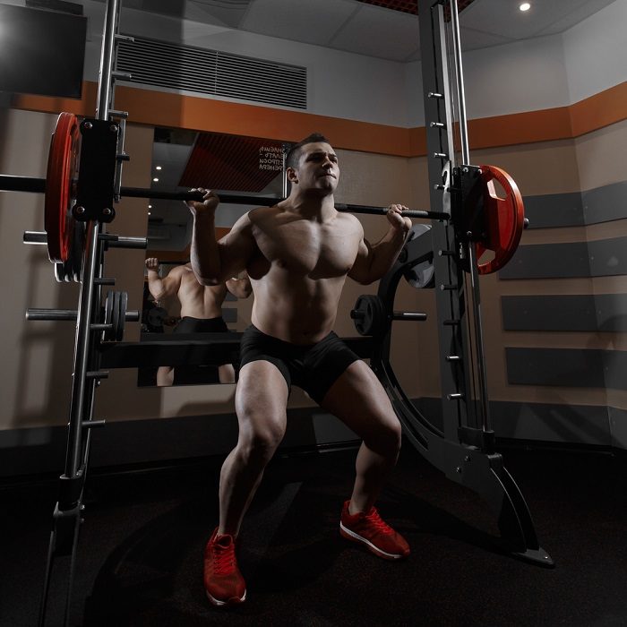 man squatting heavy barbell using smith machine