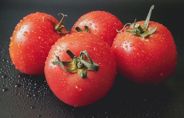 four tomatoes sprinkled with water on a black surface
