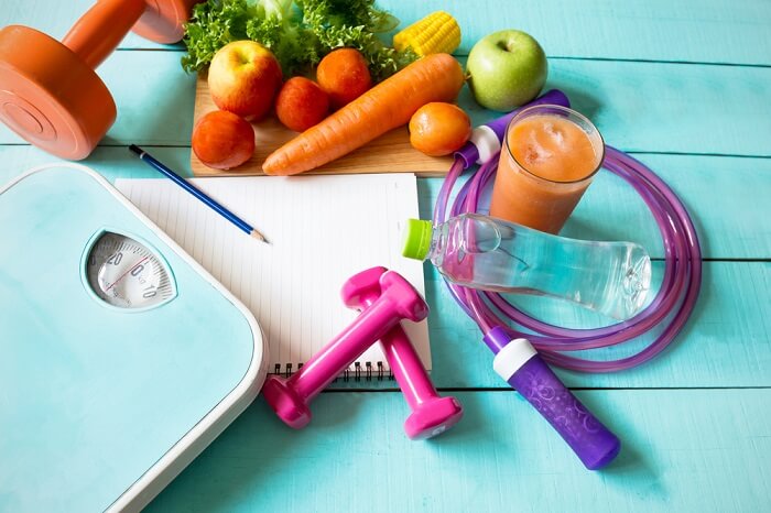fit and healthy scale, vegetables, dumbbells, jump rope and protein juice on a notebook with a pencil