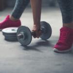 woman picking up a single dumbbell from the gym floor