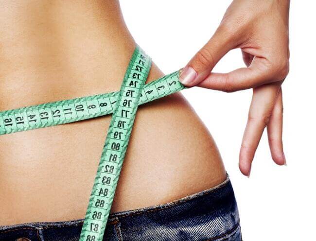 weight loss tips young fit woman holding a light blue measuring tape around her waist