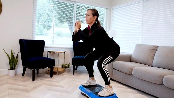 woman performing squats on vibration plate in her home