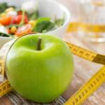 green apple, measuring tape, glass of water and a bowl of salad on a wooden surface