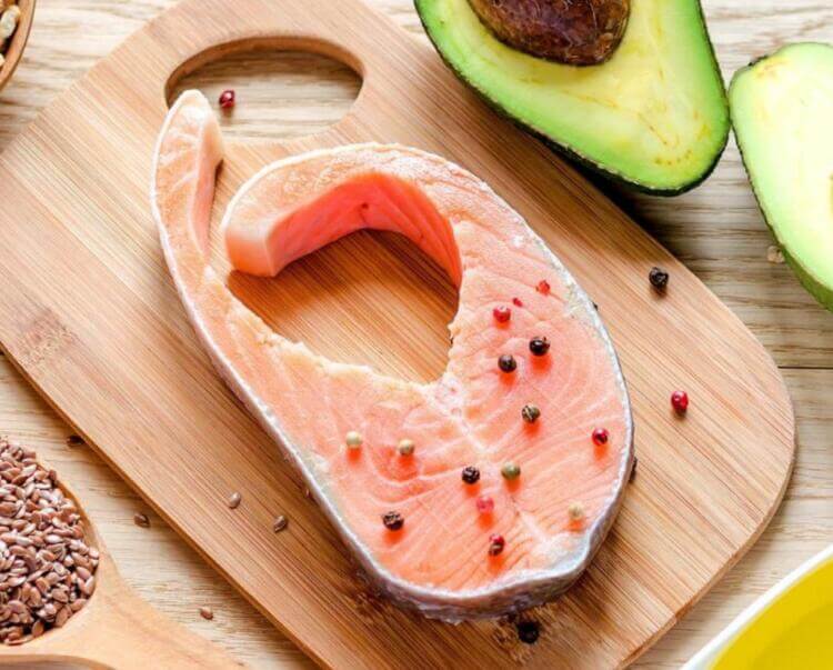piece of salmon on a cutting board next to an avocado cut in half