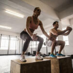 man and woman performing box jumps in a crossfit gym