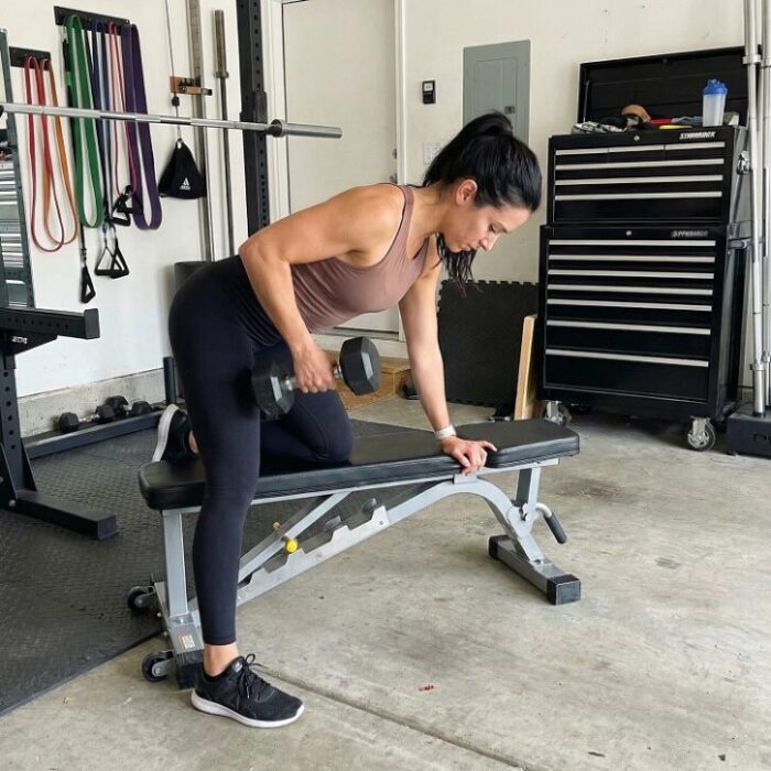 attractive woman performing tricep kickbacks in her gararge gym